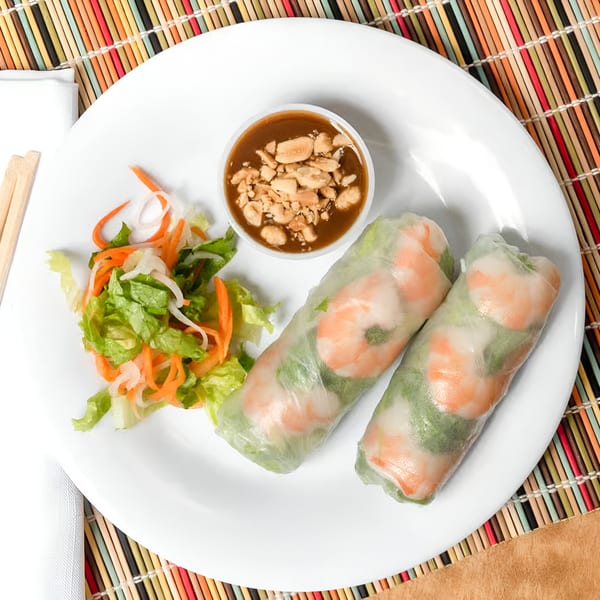 Two Vietnamese shrimp spring rolls with peanut sauce and a side salad on a white plate.