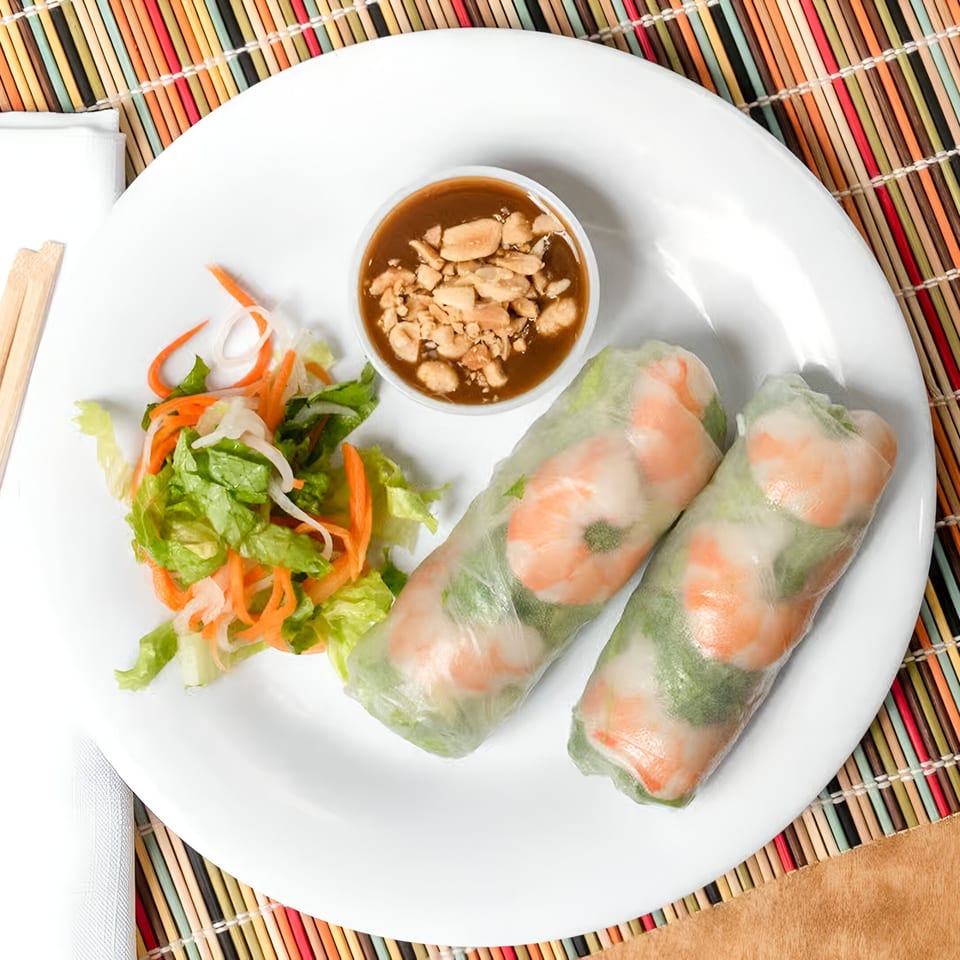 Two Vietnamese shrimp spring rolls with peanut sauce and a side salad on a white plate.