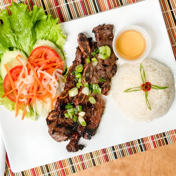 Vietnamese grilled short ribs with rice, salad, and dipping sauce on a white plate.