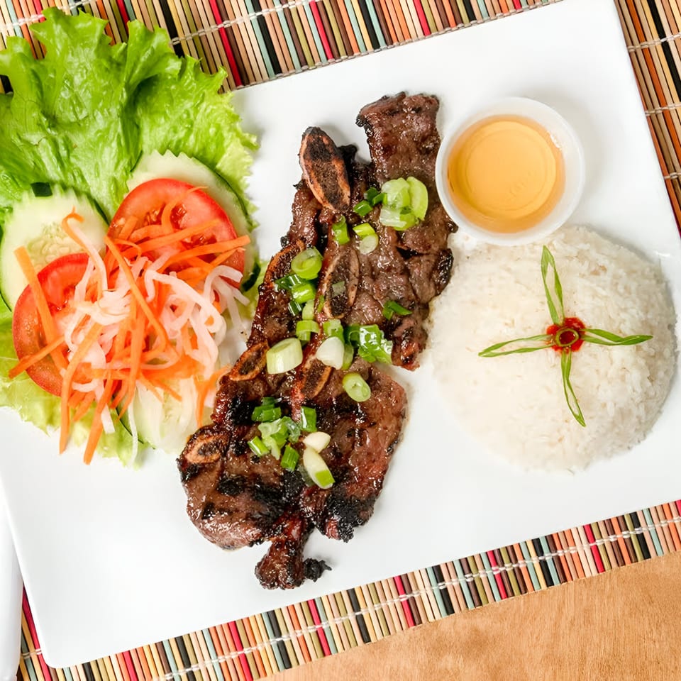 Vietnamese grilled short ribs with rice, salad, and dipping sauce on a white plate.