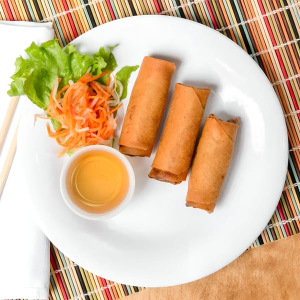 Three crispy Vietnamese egg rolls with lettuce, shredded carrots, and dipping sauce on a white plate.