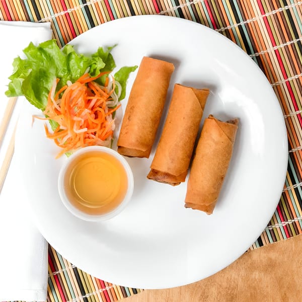 Three Vietnamese fried spring rolls with lettuce, shredded carrots, and dipping sauce on a white plate.