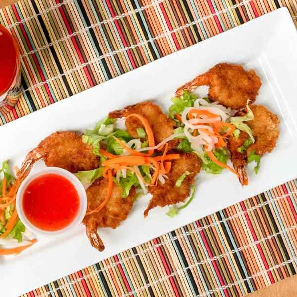 Crispy fried shrimp with sweet chili sauce, lettuce, and pickled vegetables on a white plate.