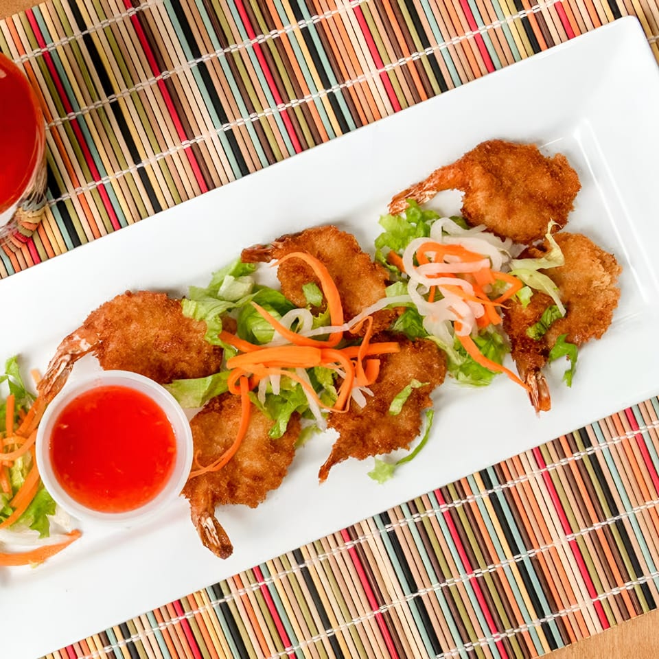 Crispy fried shrimp with sweet chili sauce, lettuce, and pickled vegetables on a white plate.
