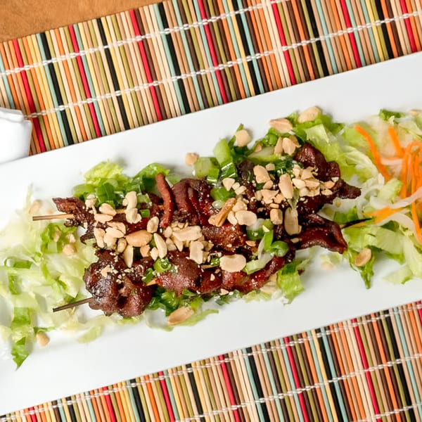 Vietnamese grilled pork skewers with peanuts and green onions on a bed of lettuce and shredded carrots.