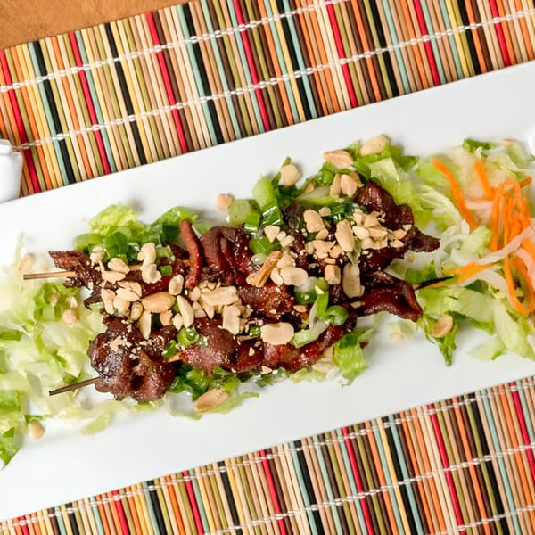 Vietnamese grilled pork skewers with peanuts and green onions, served on a bed of lettuce and pickled carrots.