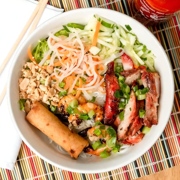 A Vietnamese vermicelli bowl with grilled pork, shrimp, egg roll, and fresh vegetables.