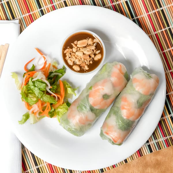 Two Vietnamese shrimp spring rolls with peanut sauce and a side salad on a white plate.