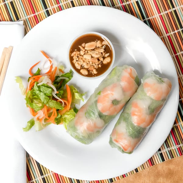 Two Vietnamese shrimp spring rolls with peanut sauce and a side salad on a white plate.