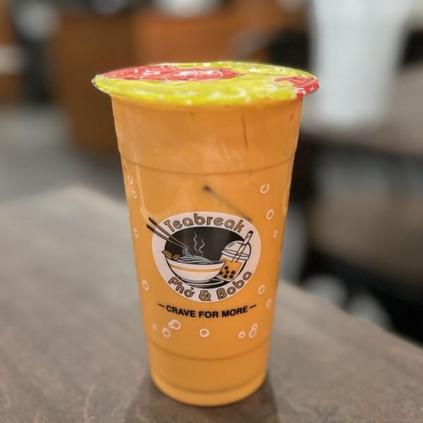 A Teabreak Pho & Boba branded cup of iced Thai tea with a red and yellow lid.