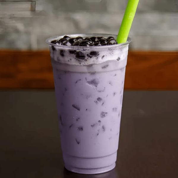 A purple taro boba tea with dark boba pearls and a green straw in a clear plastic cup.