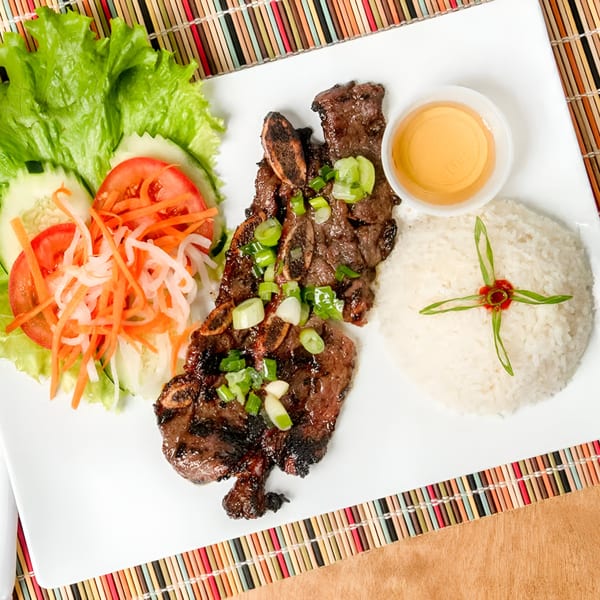 Grilled short ribs with rice, a side salad, and dipping sauce on a white plate.