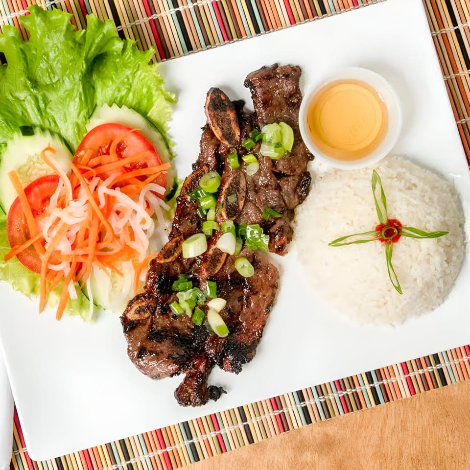 Grilled short ribs with rice, a side salad, and dipping sauce on a white plate.
